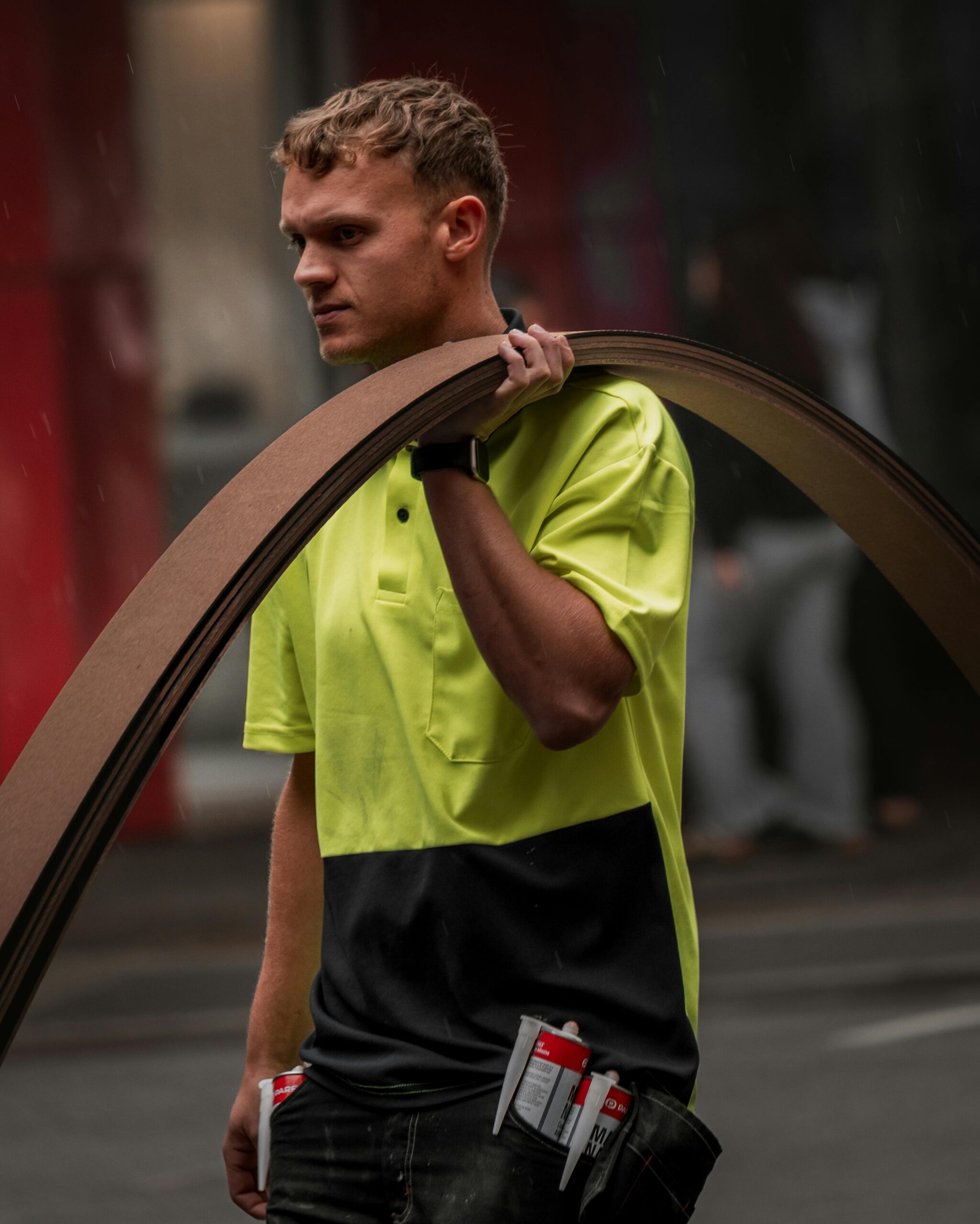 A construction worker in a neon safety vest carrying materials on a city street in Perth.