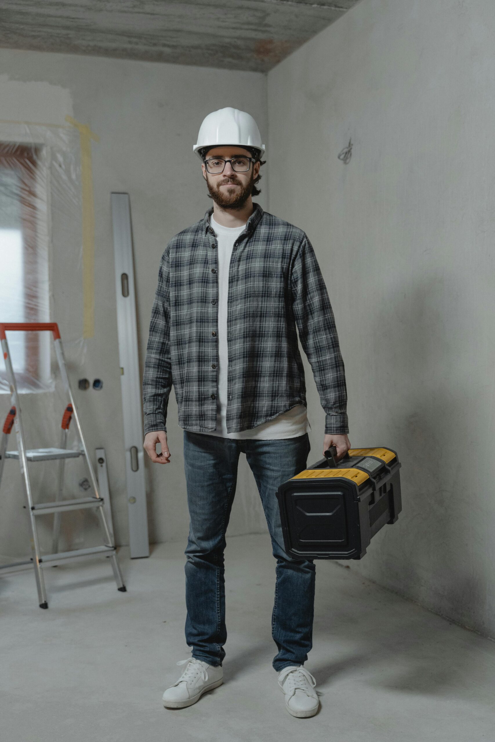 Construction worker in plaid shirt with toolbox indoors, showcasing renovation setting.